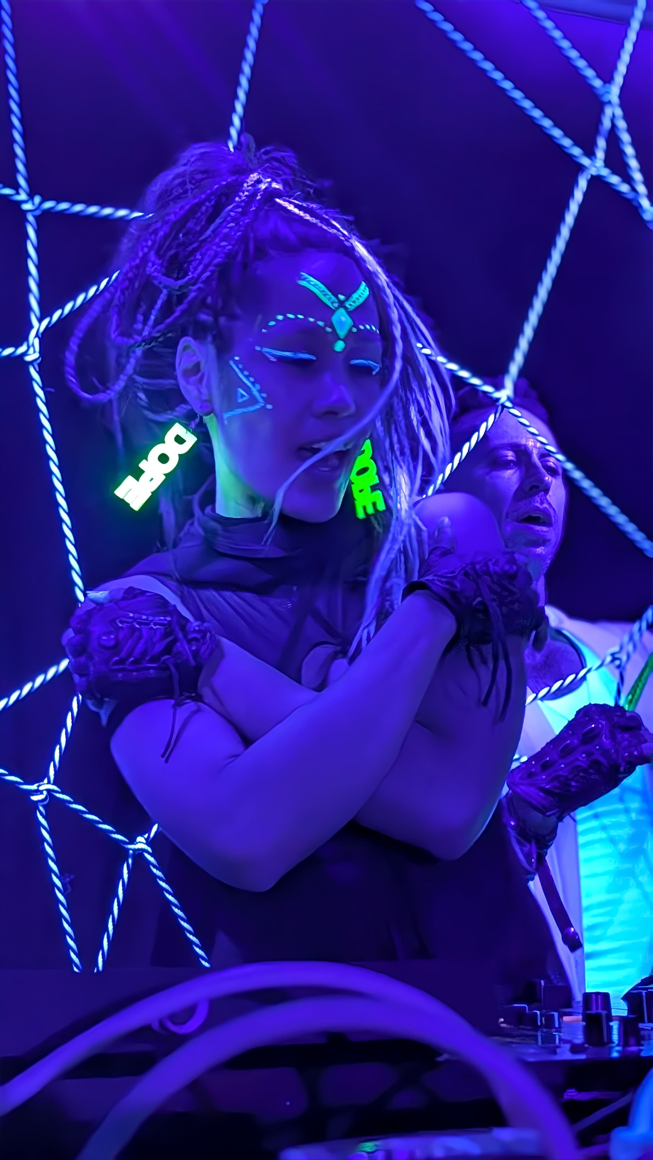Aster and Davide inside a lattice of fluorescent rope under UV light during a SUSPND performance.